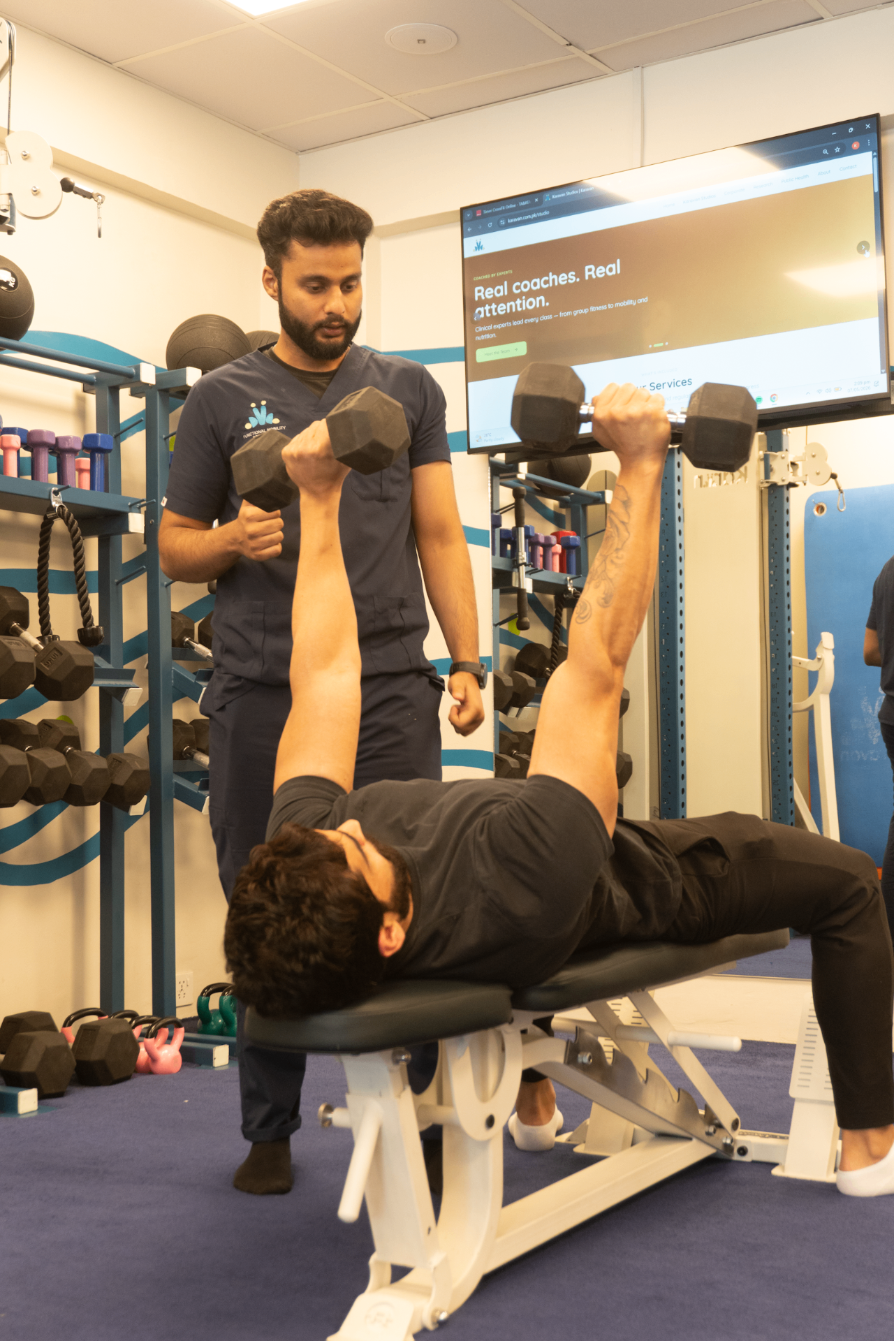 A Karavan coach supervising a member during a dumbbell bench press in the I-8 studio