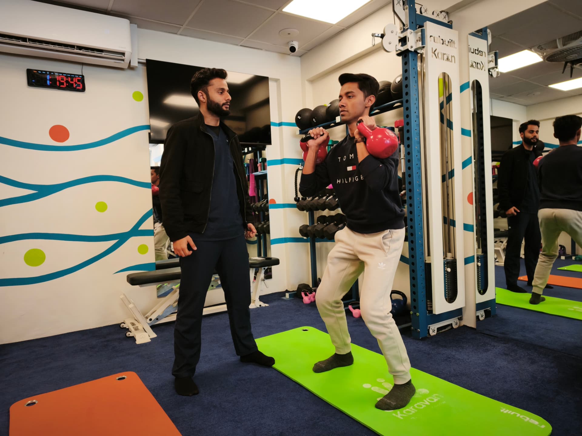 A coach supervising a member's kettlebell squat